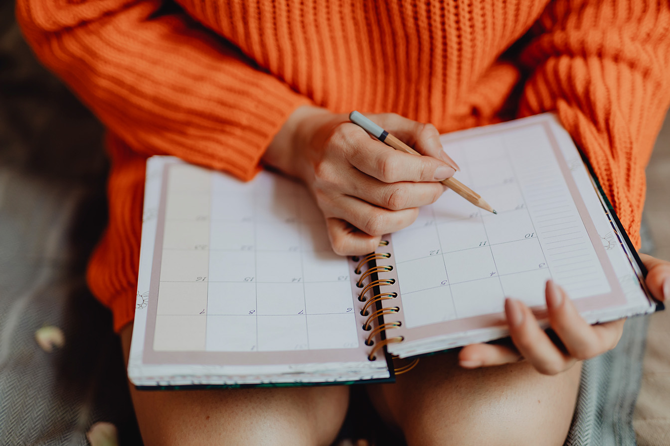 Eine Frau im orangen Pullover schreibt einen Termin in ihren Kalender.